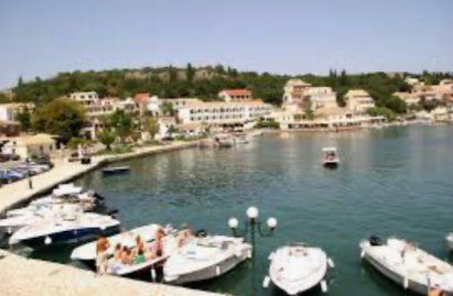 Webcam Kassiopi Marina with white boats docked beside a calm waterfront lined with buildings and trees