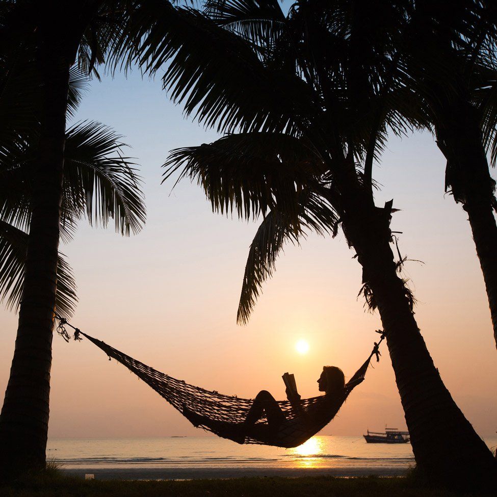A person is laying in a hammock reading a book