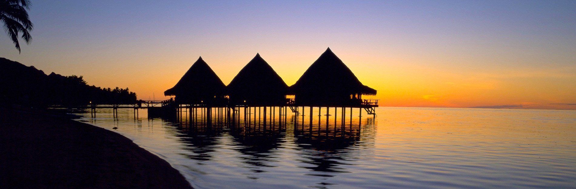 Three beach hutsare floating in the middle of the ocean at sunset.