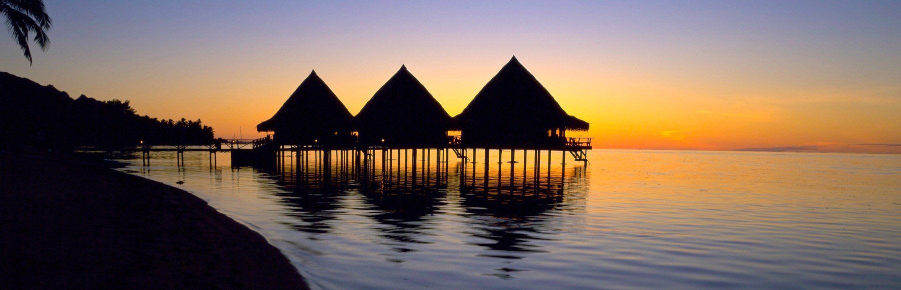 Three huts are floating in the water at sunset.
