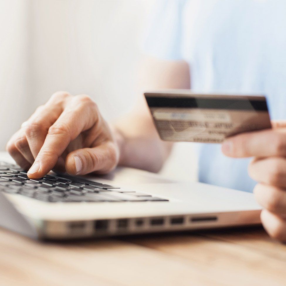 A person is typing on a laptop while holding a credit card