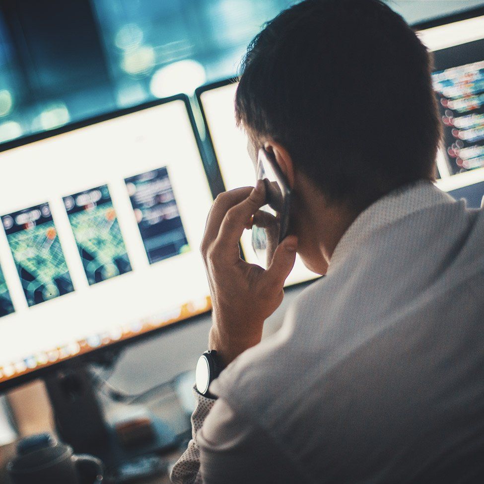 A man is talking on a cell phone in front of a computer screen.