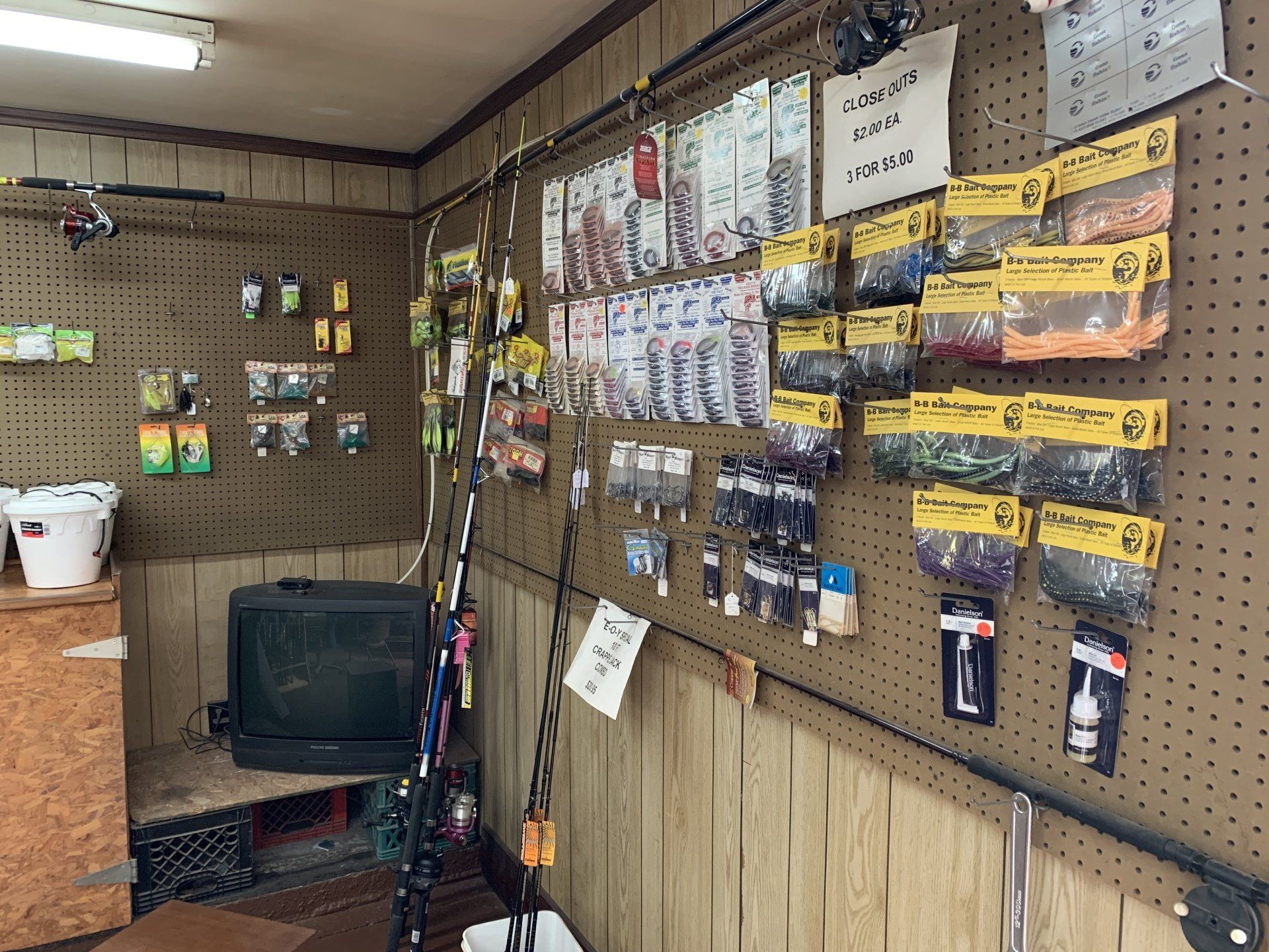 Interior of a small tackle shop. Fishing rods, lures, and bait displayed on pegboard walls. A TV sits on a shelf.