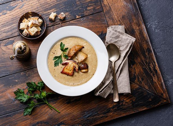 Eine Schüssel Suppe mit Croutons und einem Löffel auf einem Holztisch.