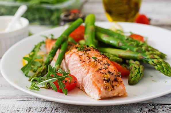 Ein weißer Teller mit Lachs, Spargel und Tomaten.