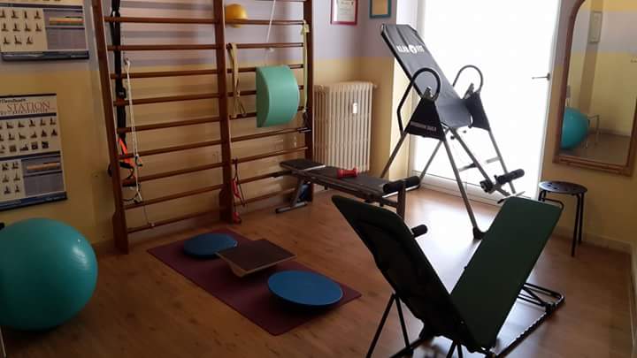 Sala di fisioterapia con attrezzatura per esercizi: tavolo da inversione, spalliera, attrezzi per l'equilibrio, palla da ginnastica.