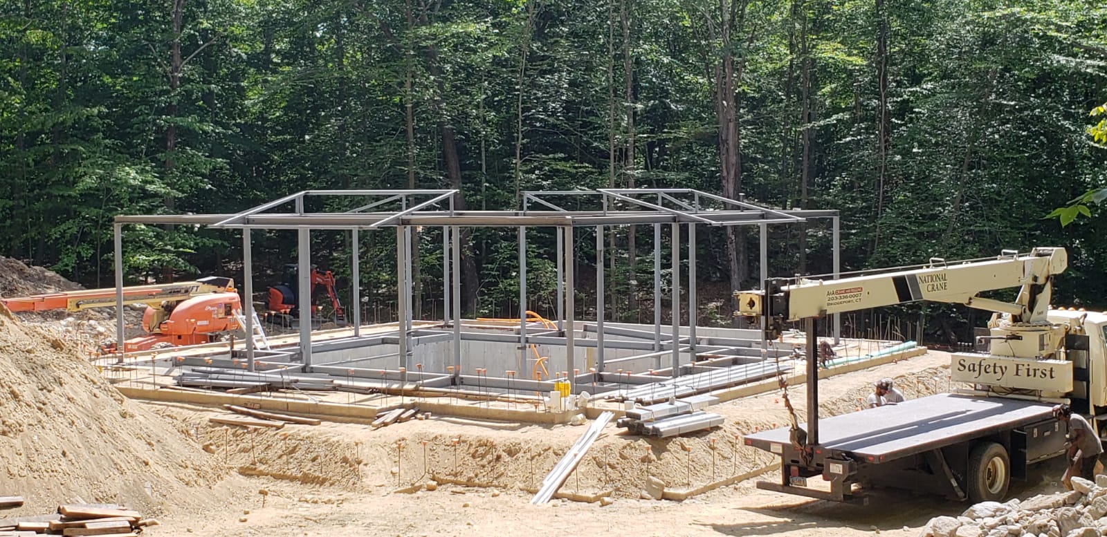Construction site with a steel frame structure, crane, and surrounding trees.