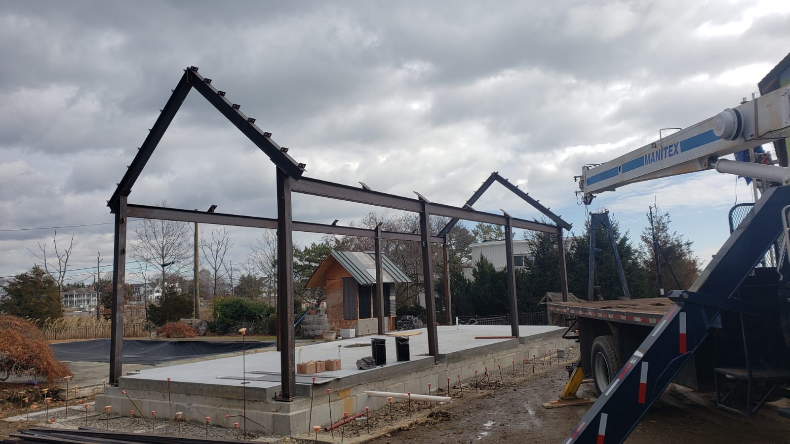 Construction site with a metal frame being erected by a crane. Cloudy sky.