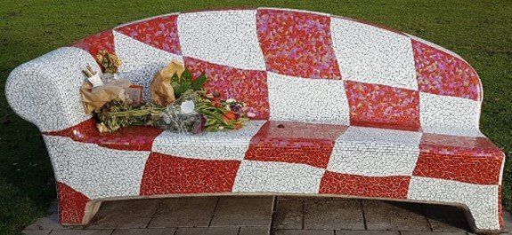 Een rood-wit geblokte bank met bloemen en een speeltje erop, die buiten staat.
