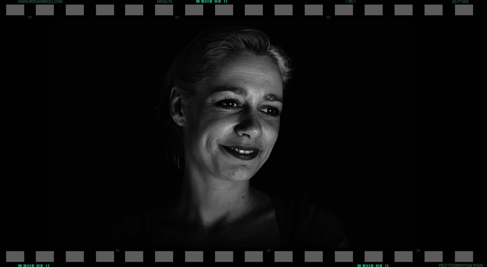 Vrouw glimlacht in een donkere omgeving, van onderaf verlicht; zwart-wit filmbeeld.
