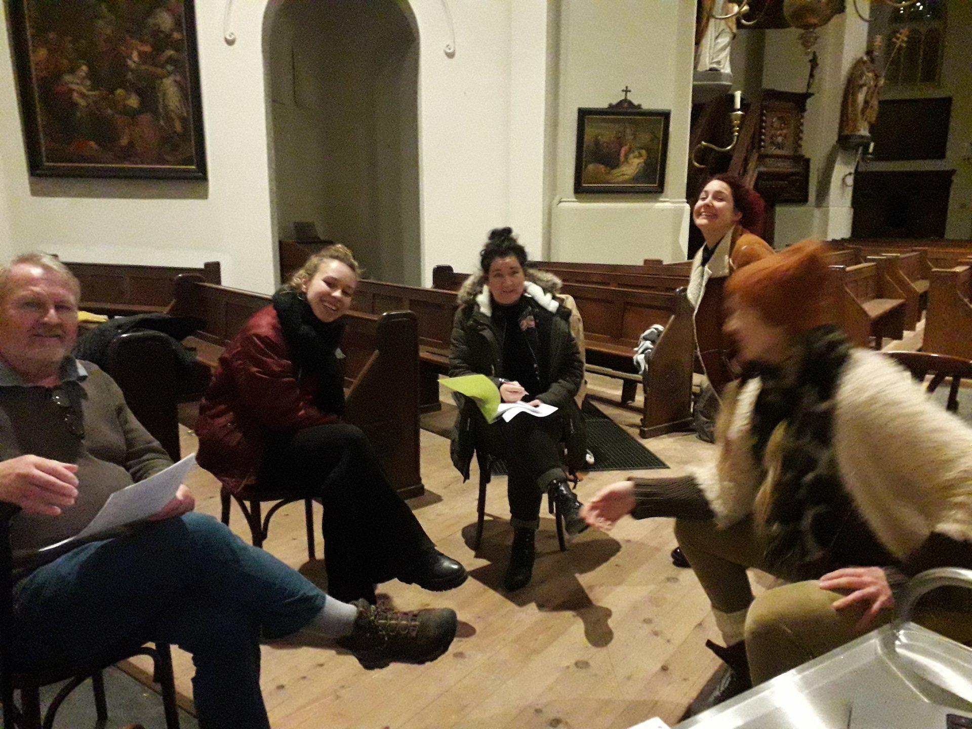 Mensen in een kerk, verzameld in een kring. Ze glimlachen en praten, sommigen houden papieren vast.