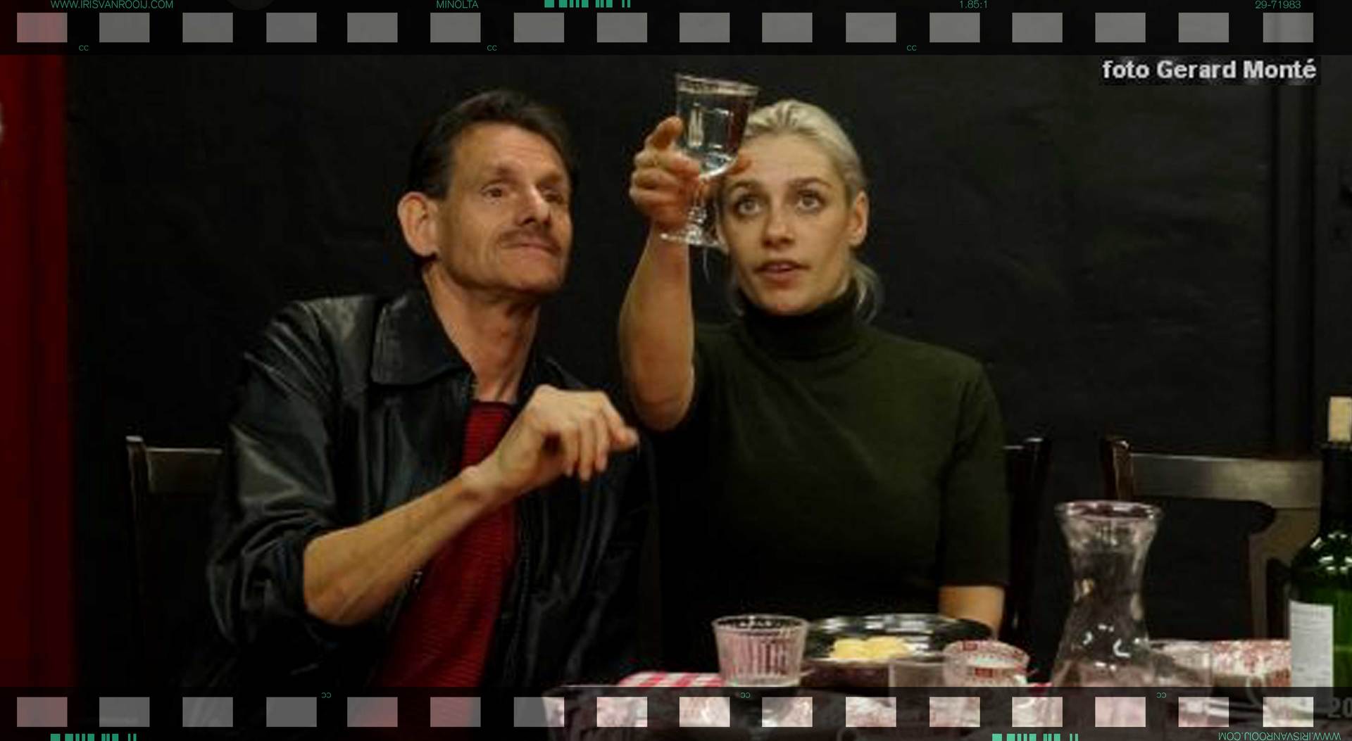 Een man en een vrouw zitten aan tafel, de vrouw houdt een glas omhoog en kijkt omhoog.