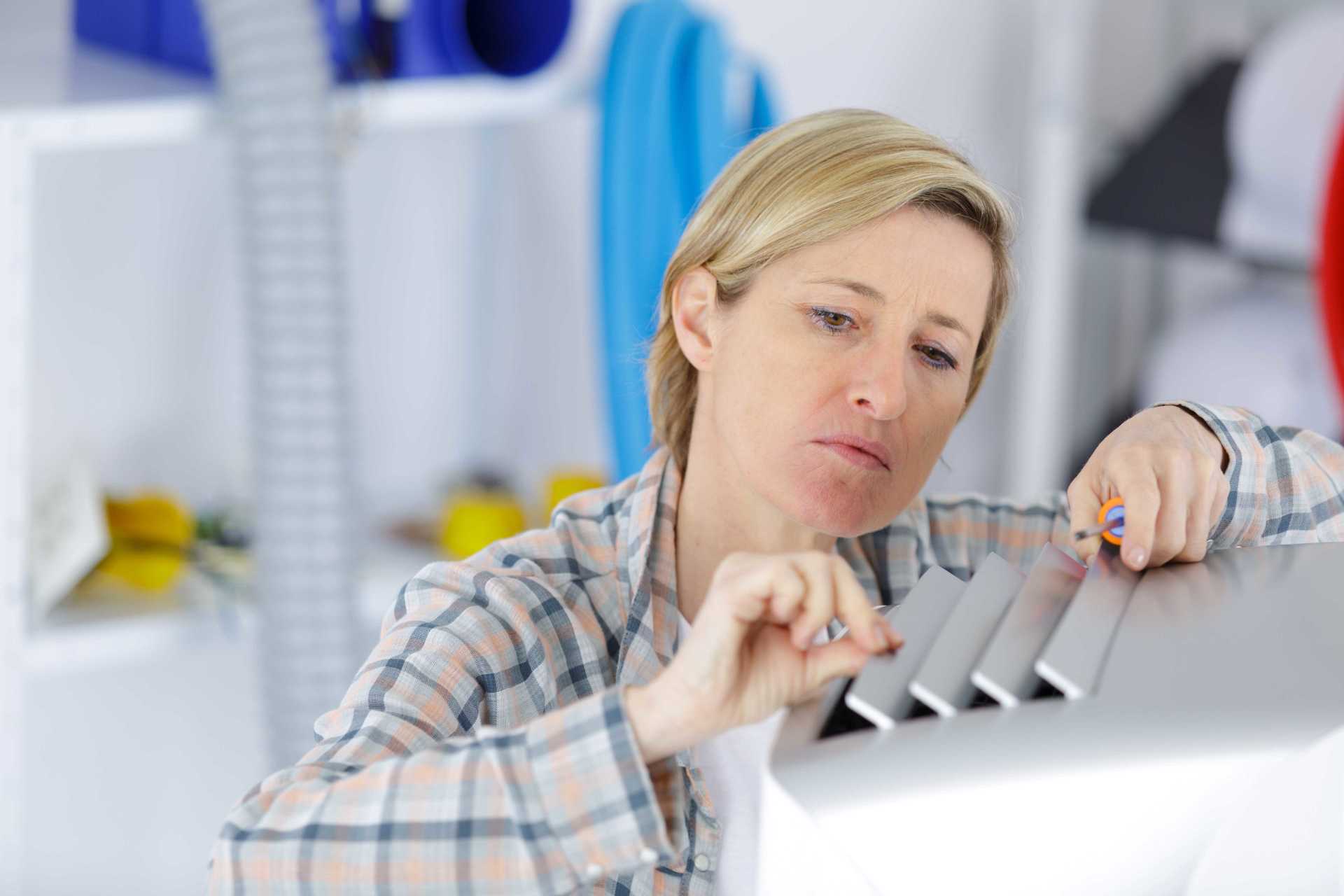 Woman inspecting a white appliance with a small screwdriver in a bright room