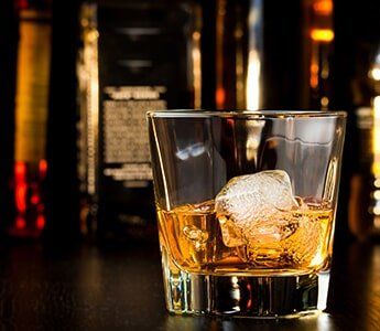 Whiskey Glass With Ice in Front of Bottles — Liquor Store in Wilmington, DE