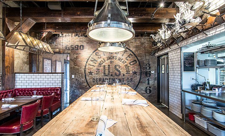 a long wooden table in a restaurant with a u.s. department of meat stamp on the wall at uncle jacks meathouse