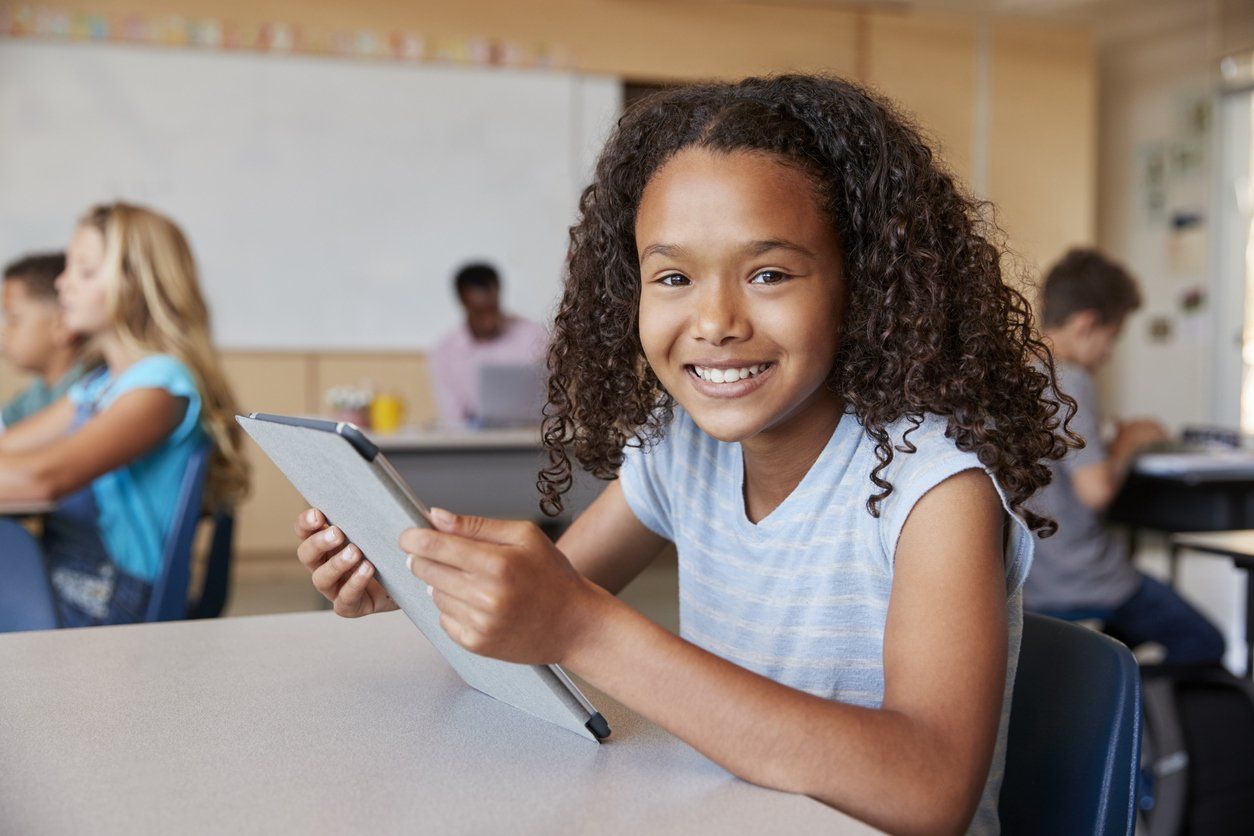 a young girl is smiling while holding a tablet in a classroom