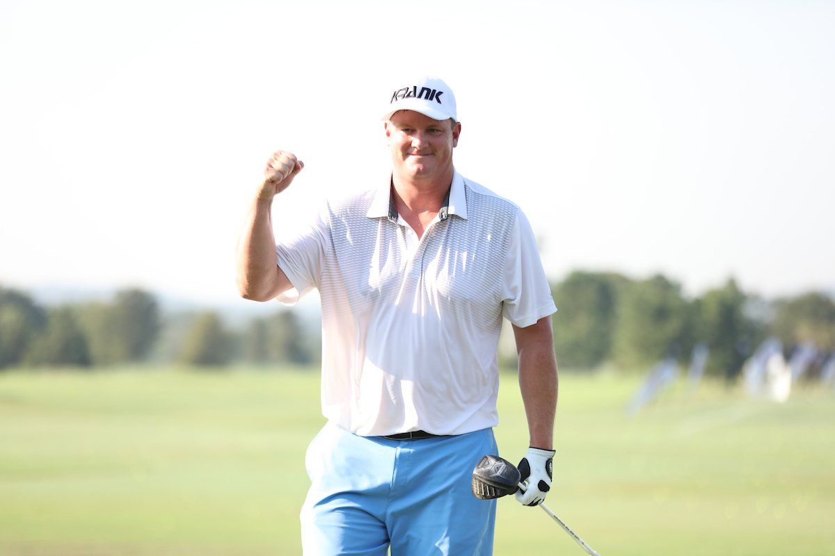 A man in a white shirt and blue shorts is holding a golf club