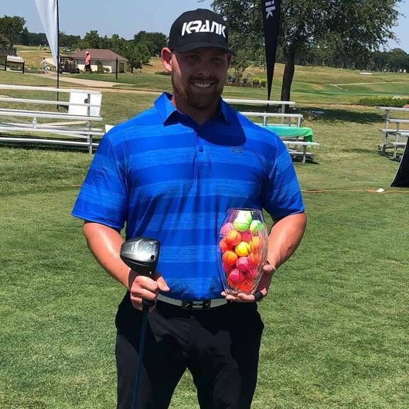 Man in blue shirt and black hat holding golf club and colorful balls on a course.