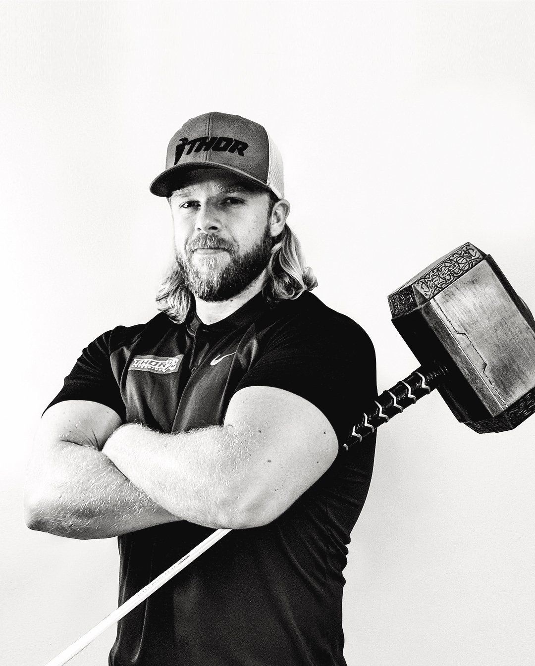 A man is holding a hammer with his arms crossed in a black and white photo.