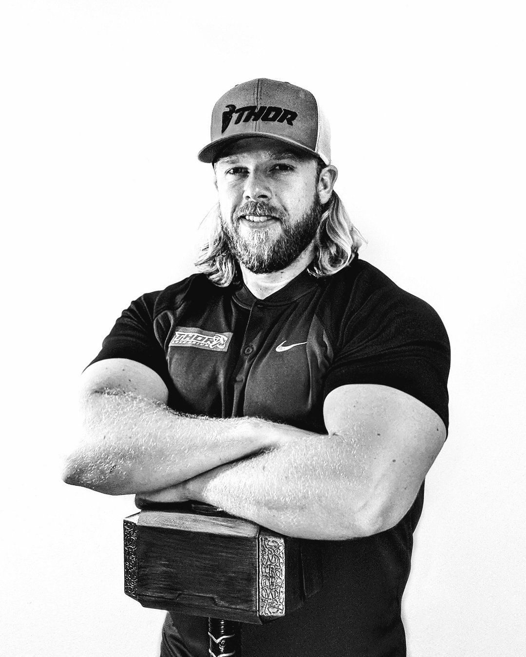 A man with a beard is standing with his arms crossed and holding a dumbbell.