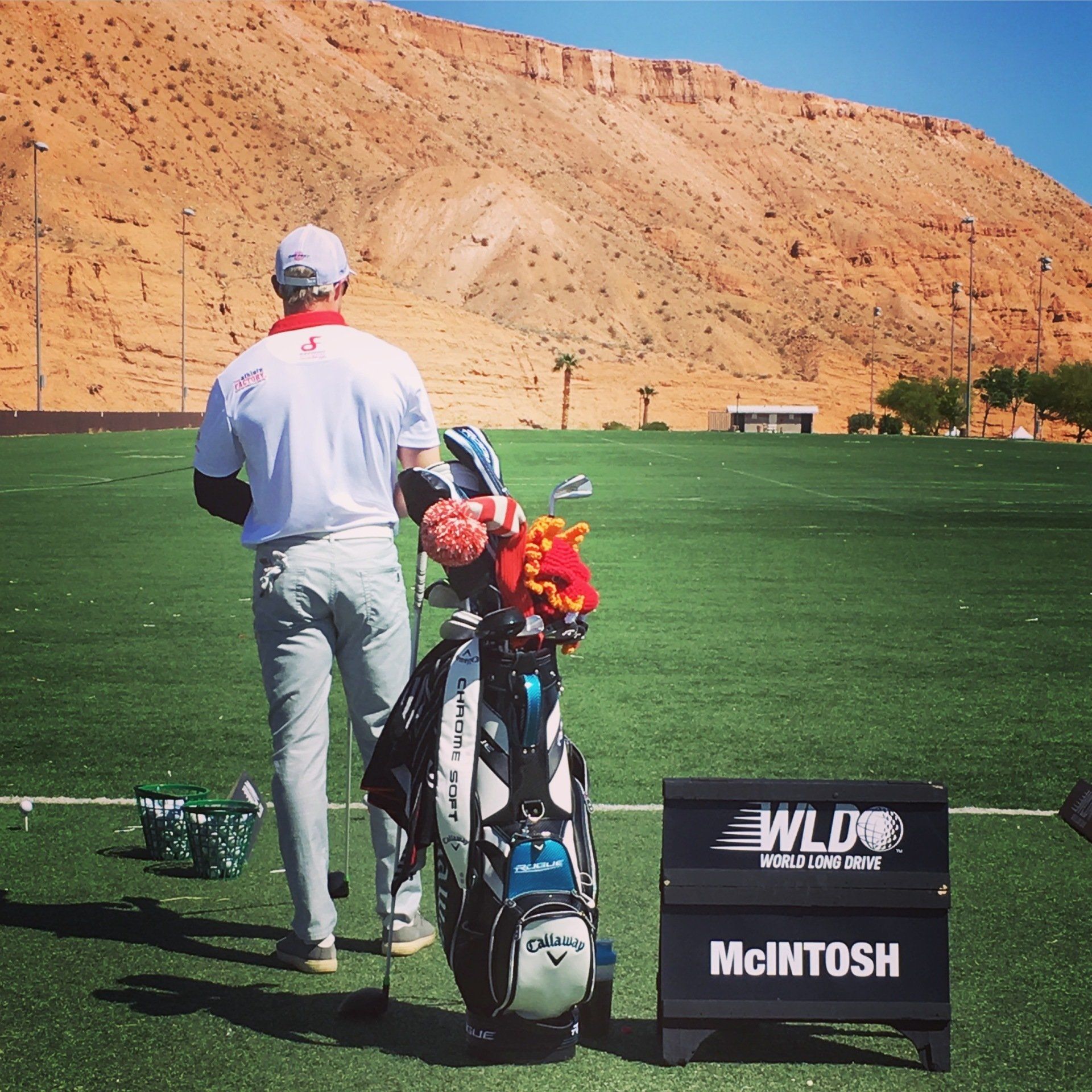A man carrying a golf bag is standing next to a sign that says mcintosh