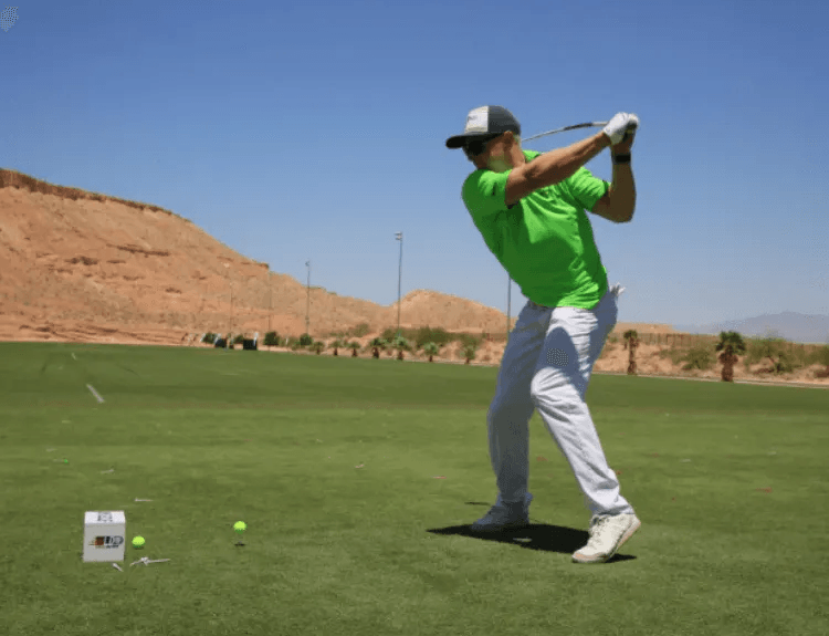 A man in a green shirt is swinging a golf club on a golf course