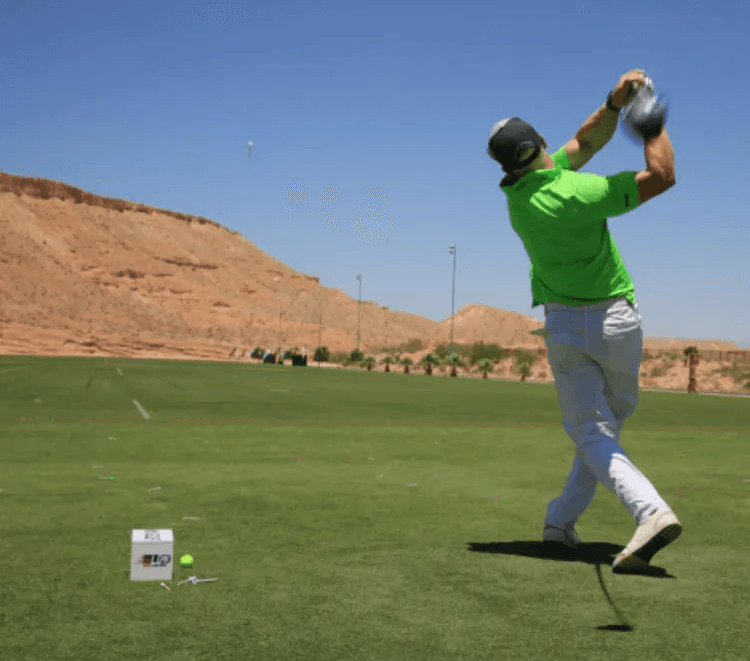 A man in a green shirt is swinging a golf club