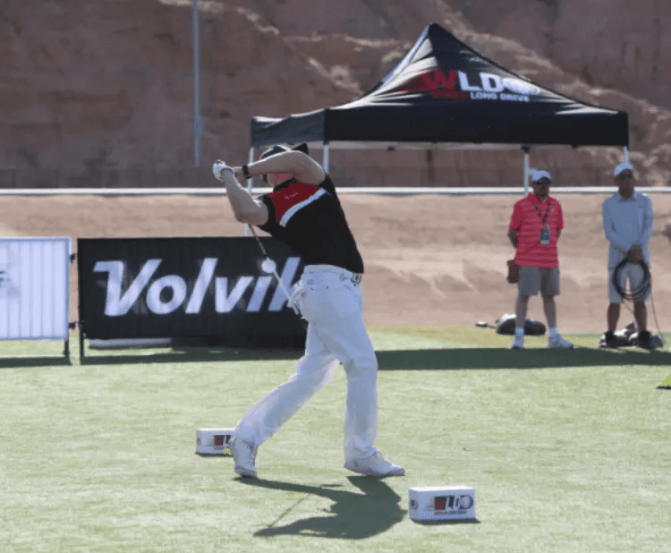 A man swings a golf club in front of a banner that says volvik