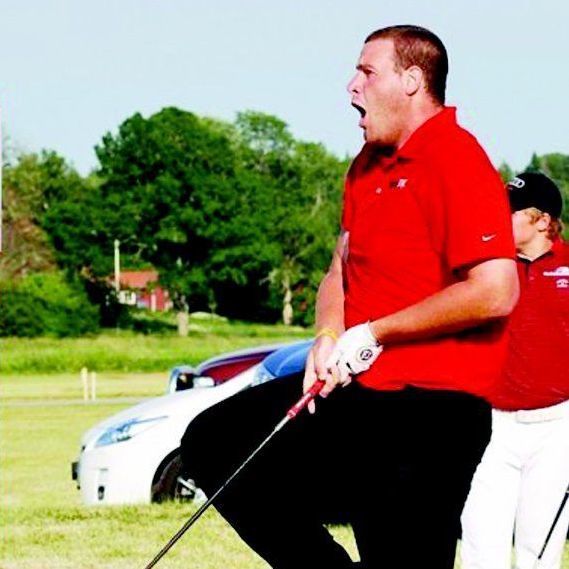 A man in a red shirt is holding a golf club