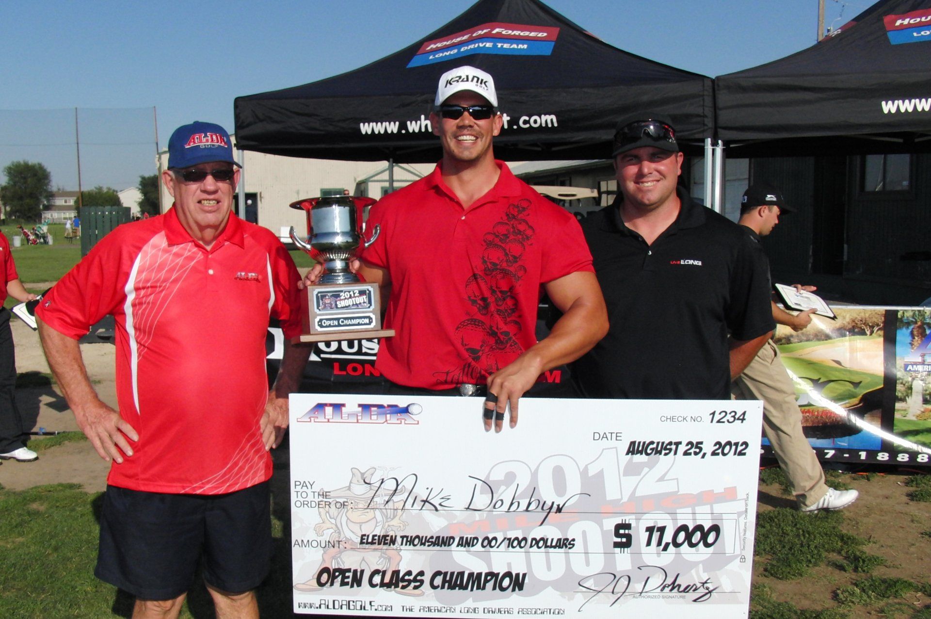 A man in a red shirt is holding a check for $ 11,000