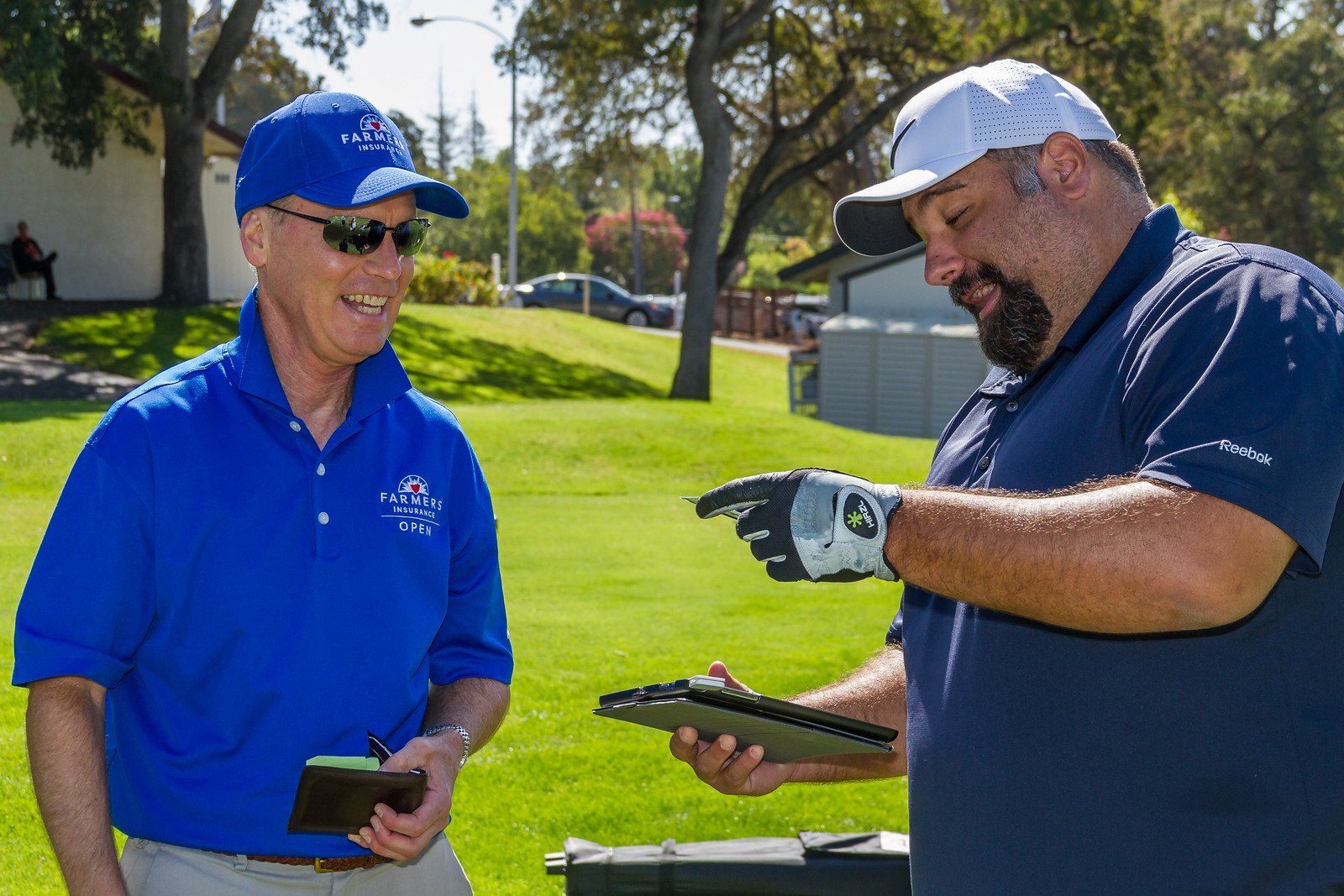 Two men are standing on a golf course talking to each other.