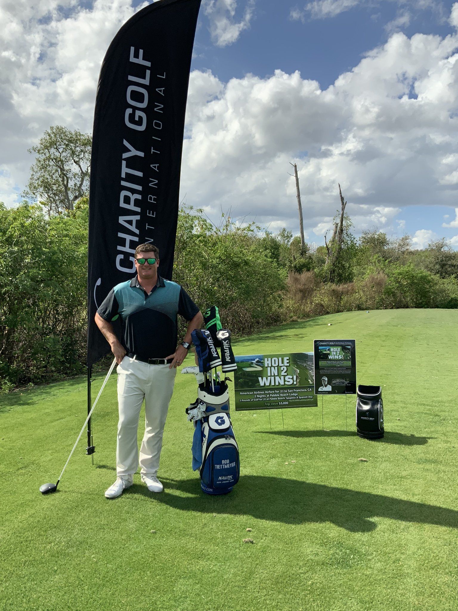 A man is standing on a golf course with a golf club and bag.