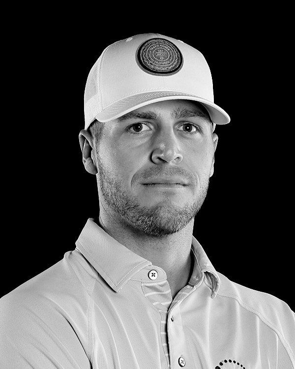 Man in cap, smiling slightly, wearing a light-colored collared shirt, black background.