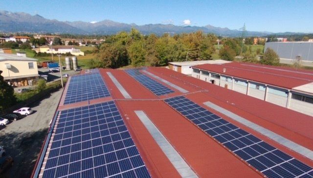Veduta aerea di un tetto industriale rosso con diverse file di pannelli solari blu scuro
