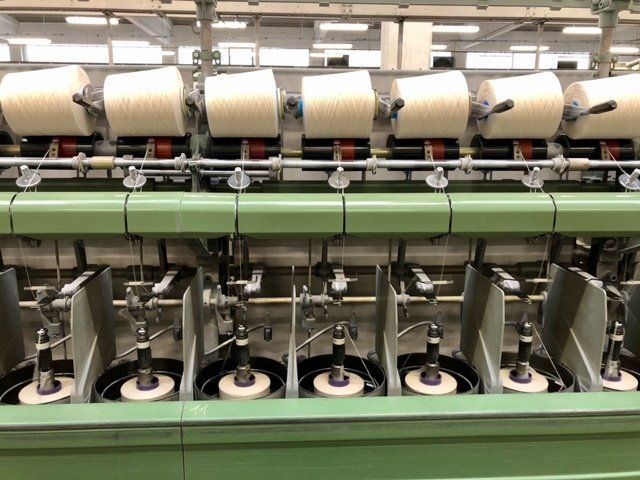 Una fila di bobine di filato bianco su una macchina per la filatura tessile industriale in un contesto di fabbrica.