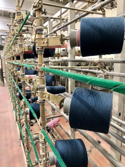 Primo piano di un portarocchetti industriale tessile con diverse bobine di filato blu scuro disposte in file