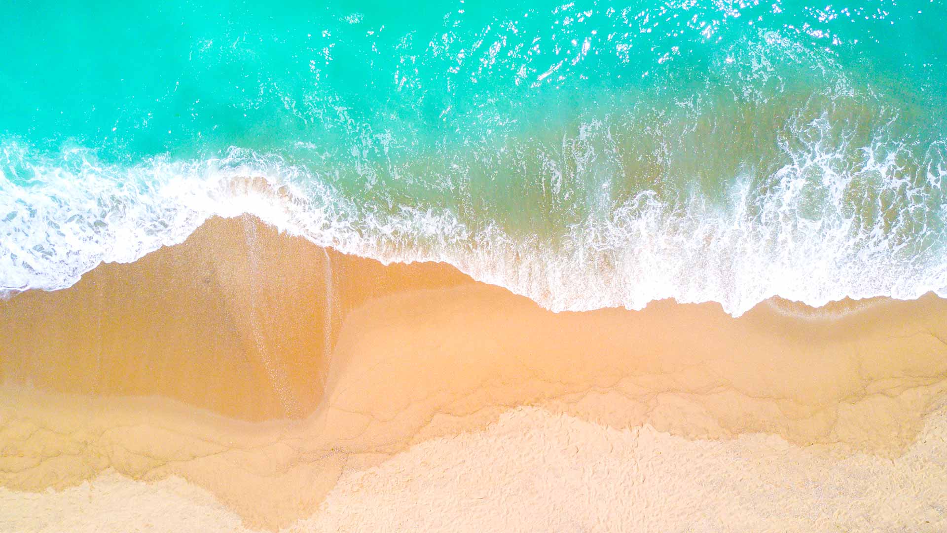 Aerial view of a sandy beach with turquoise ocean waves crashing onto the shore.
