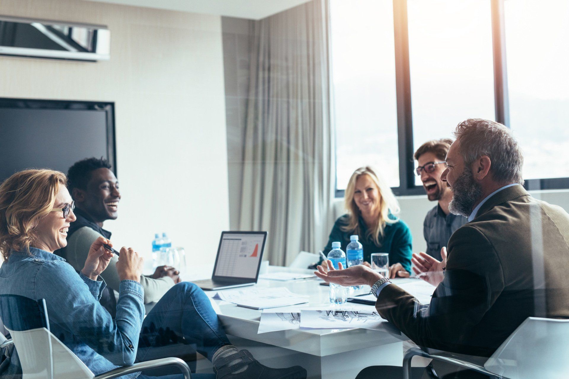 People gathered around a conference table in an office, discussing documents with a laptop present.
