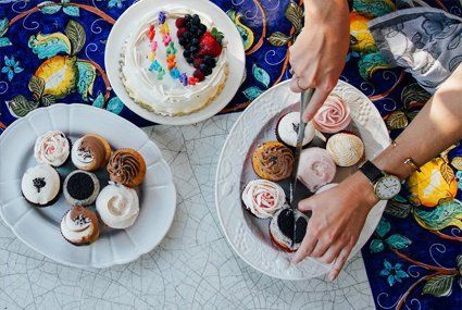A person is cutting cupcakes on a plate next to a cake on a table.