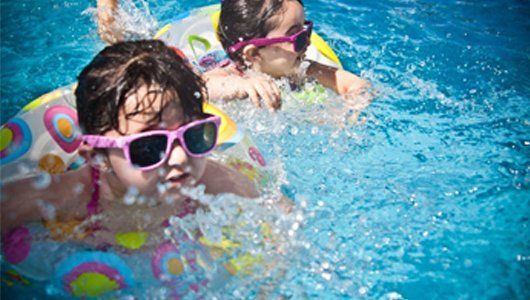 Two young girls wearing sunglasses are swimming in a pool.