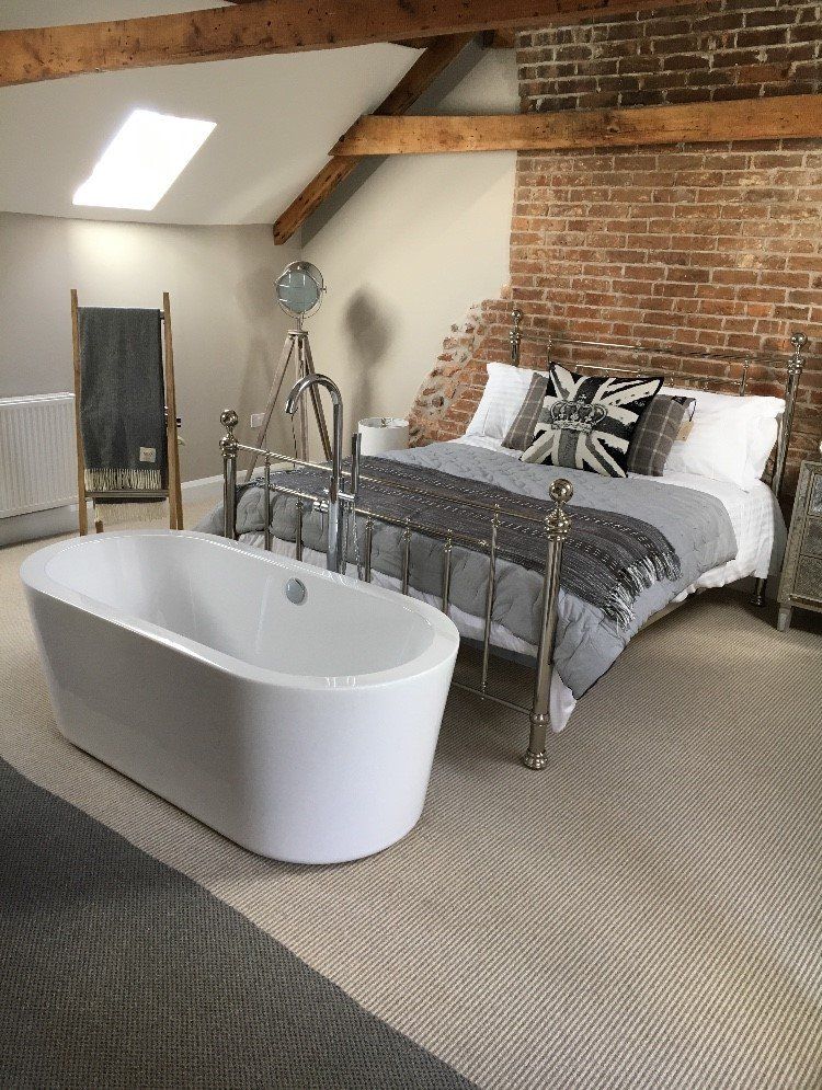 Loft bedroom with exposed brick, metal bed, freestanding bathtub, and skylight on a woven rug.