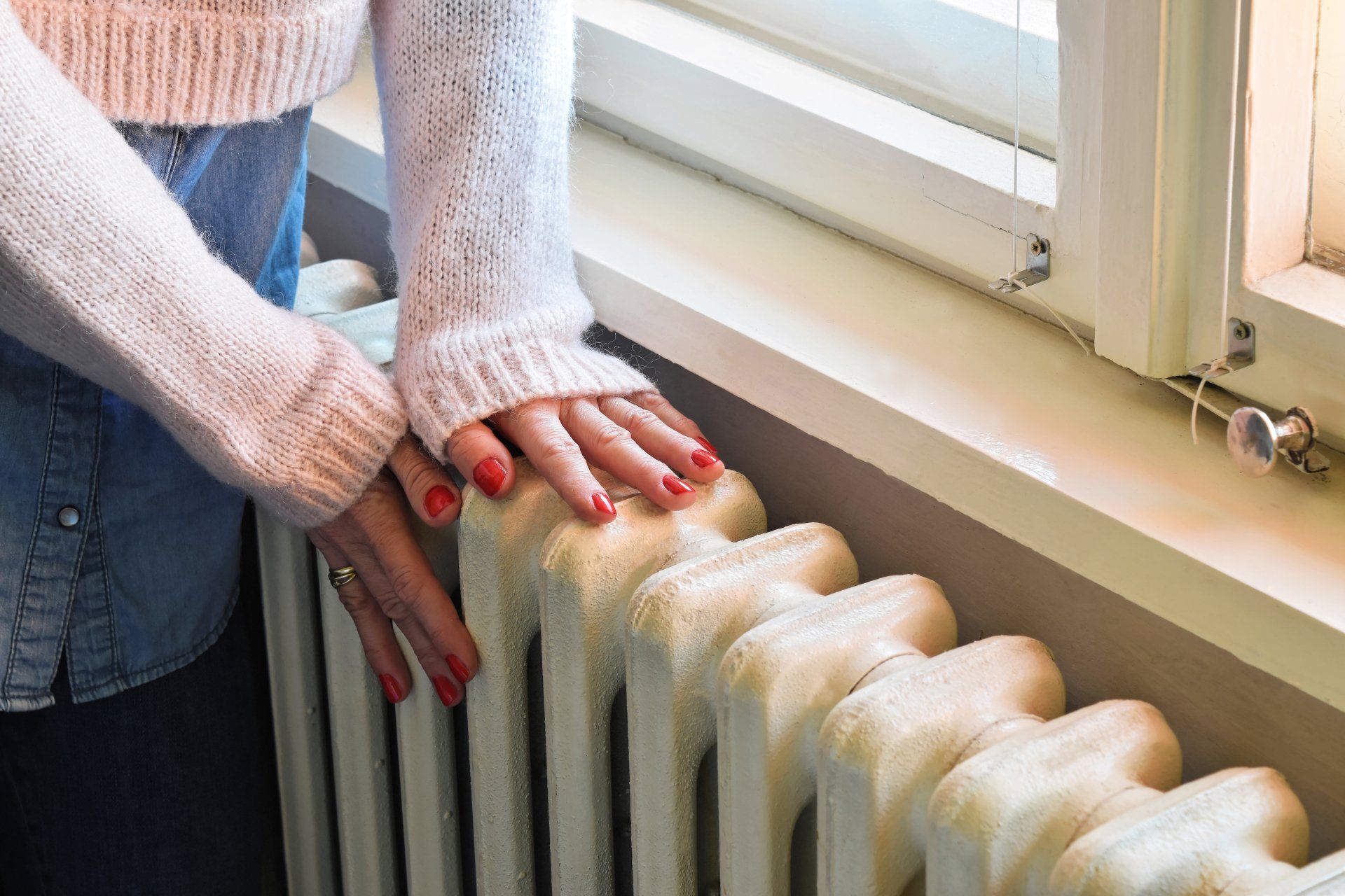 Hands in pink sweater resting on a white radiator by a window