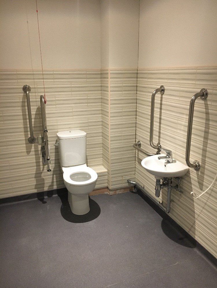 Accessible restroom with toilet, wall-mounted sink, and grab bars on beige tiled walls.