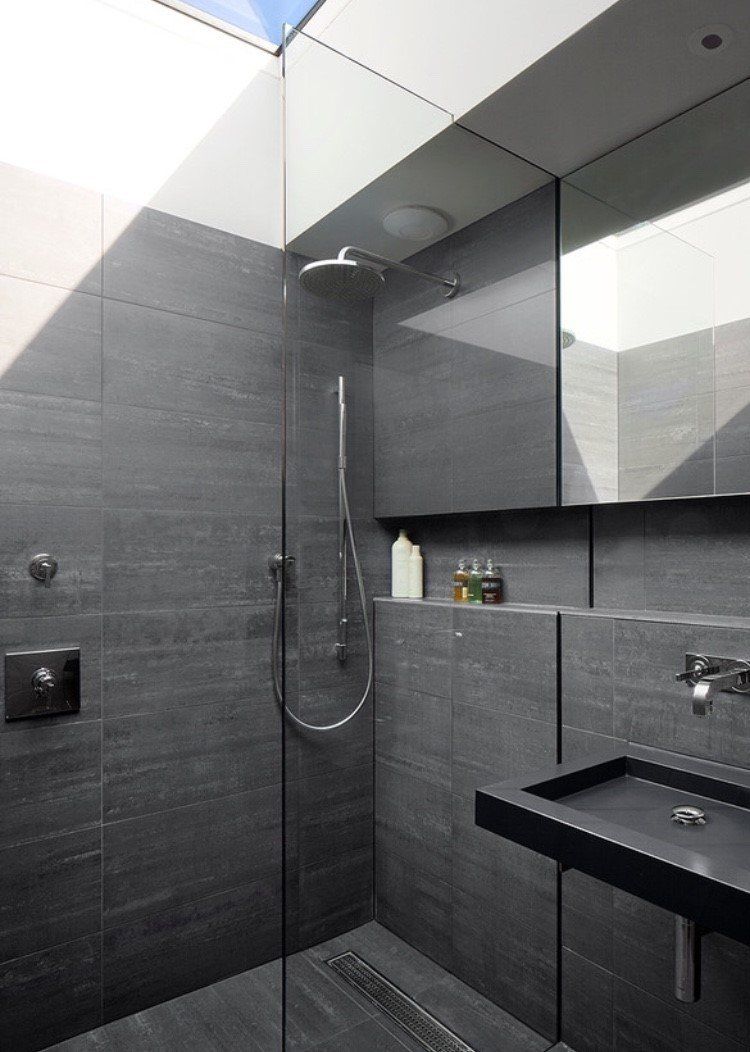 Modern dark-gray tiled shower with glass panel, handheld showerhead, and wall-mounted sink in a compact bathroom