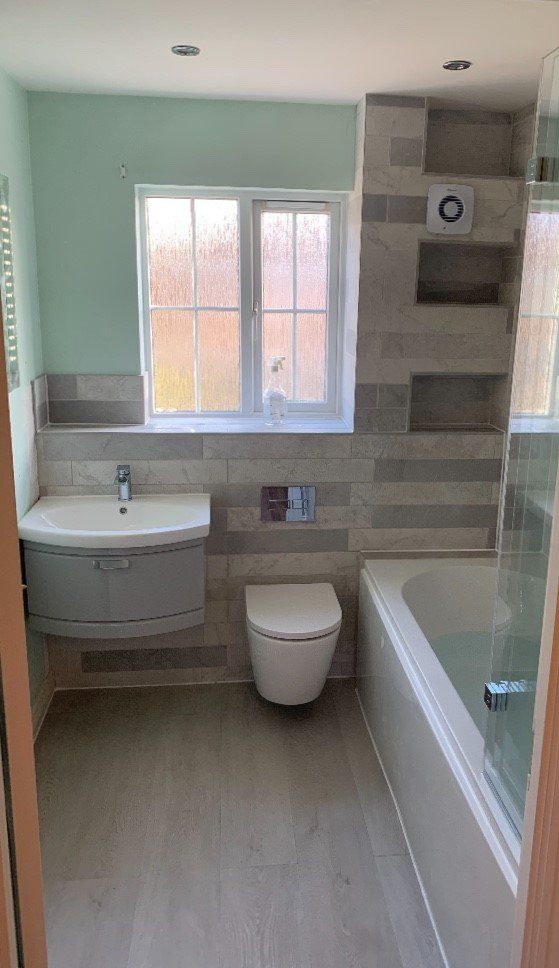 Bright modern bathroom with window, sink, toilet, and bathtub in light green and beige tones