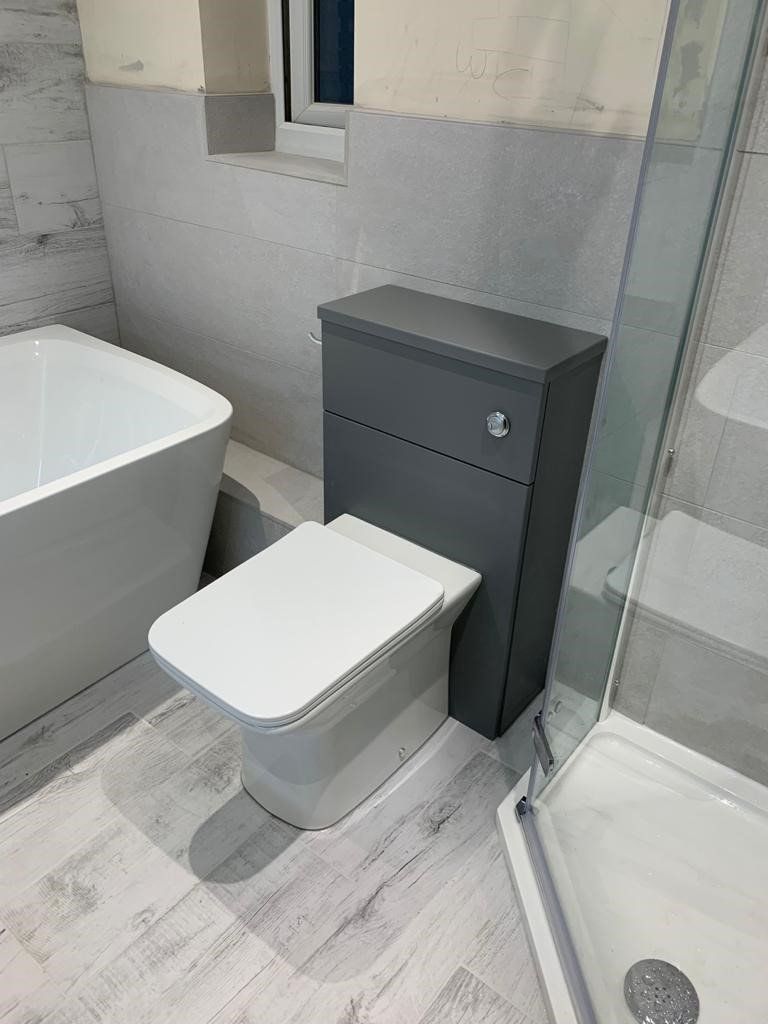 Small bathroom with white toilet, dark gray cabinet, tub, and glass shower enclosure.