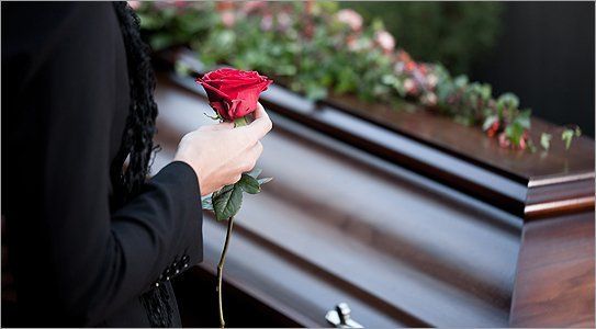 A woman holding a rose beside a coffin