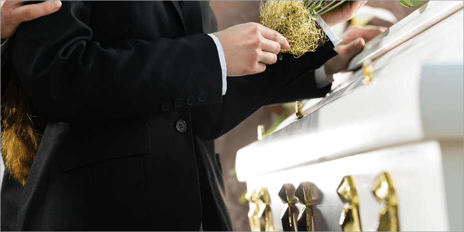 A woman standing with her hand on a white coffin, another arm comfortingly around her shoulder