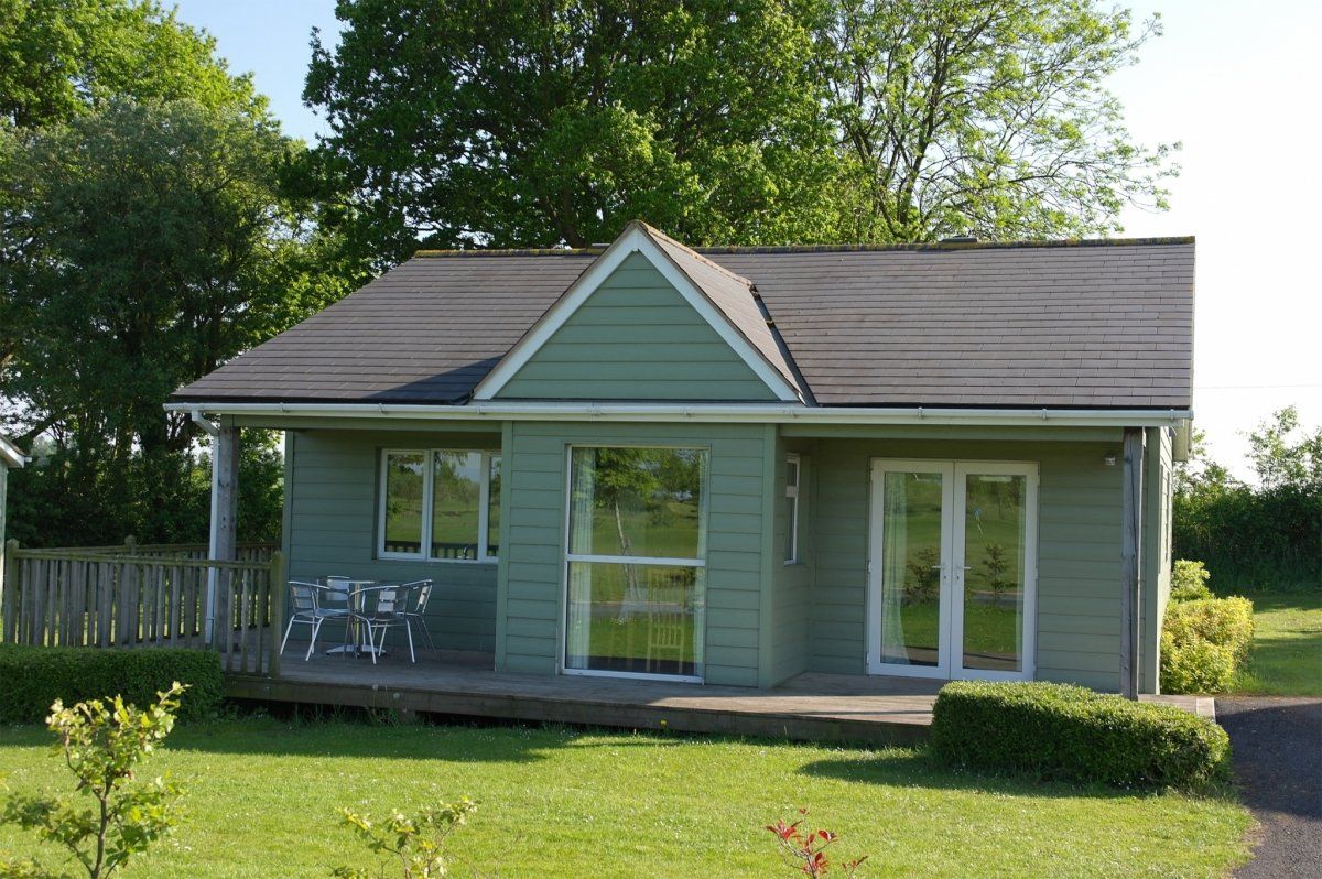 A small green house with a black roof is sitting in the middle of a lush green field.