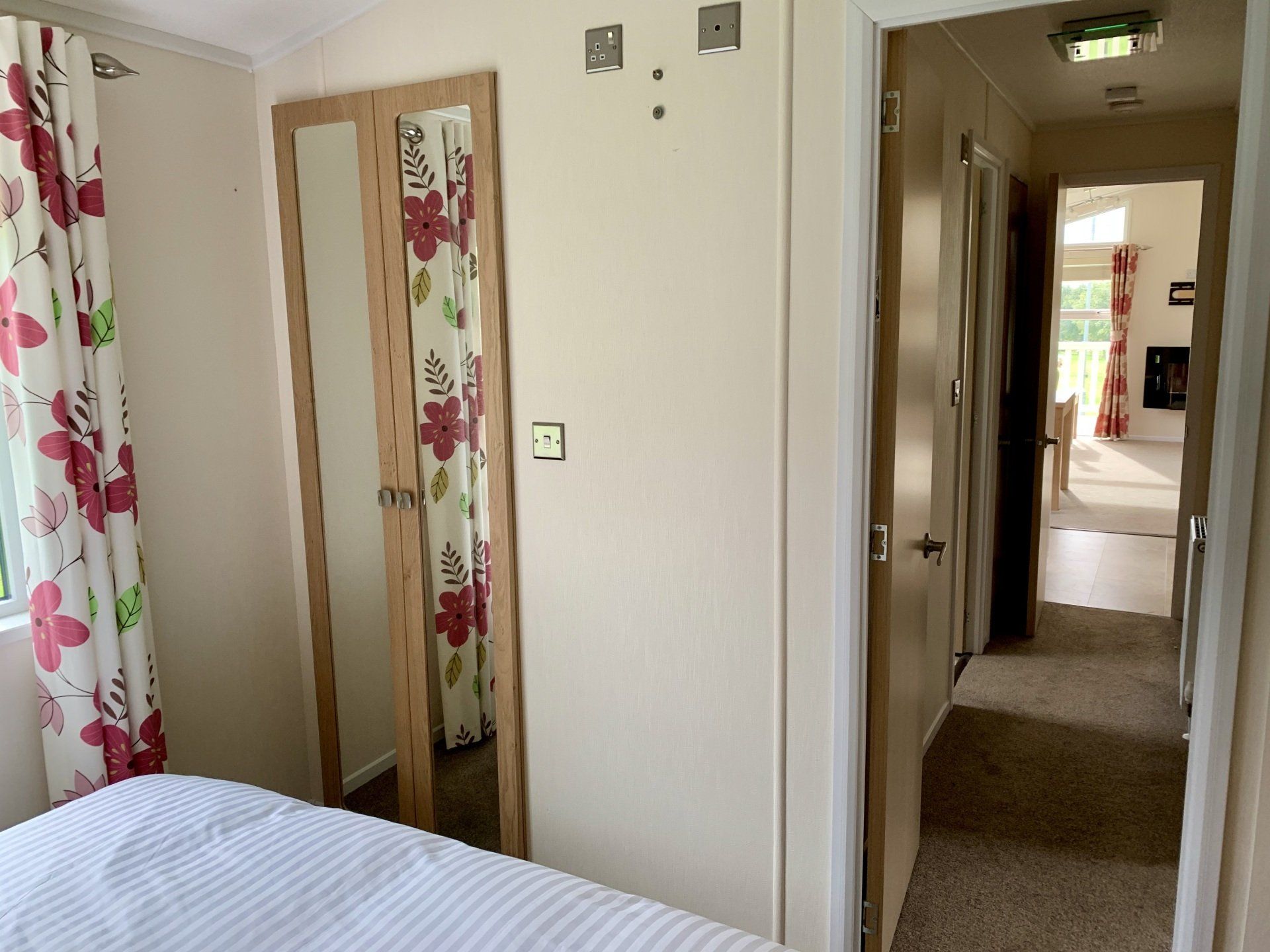 A bedroom with a bed , mirror , curtains and a hallway
